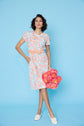 Woman in a floral dress holding flowers against a blue background