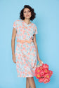 Woman wearing a floral dress holding pink flowers against a blue background